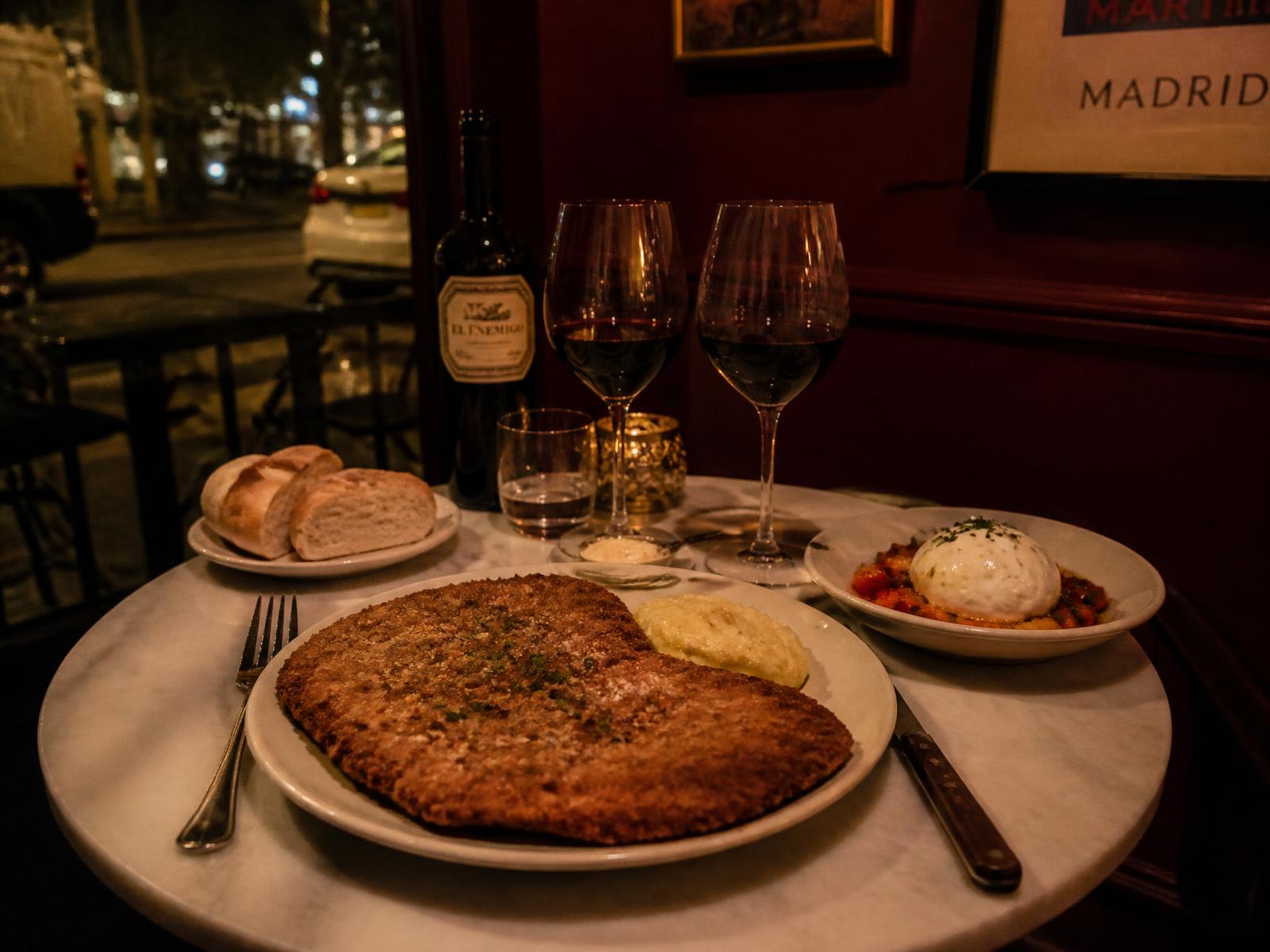 Mesa con milanesa, burrata y dos copas de vino tinto en Querido Martínez